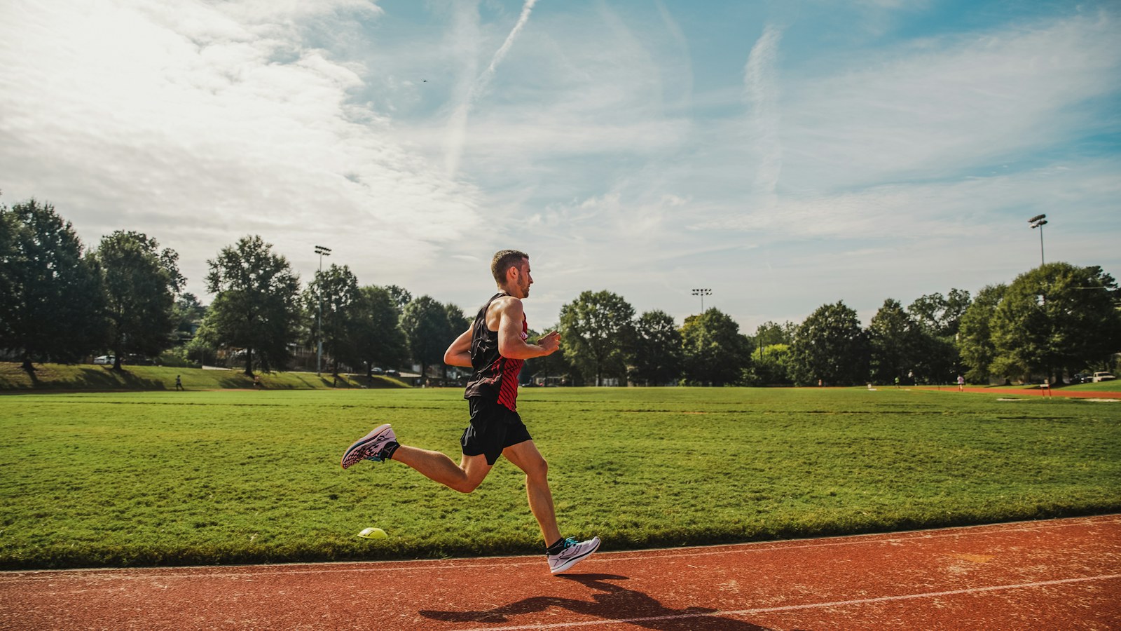 Runner training on a red athletics track beside a green field